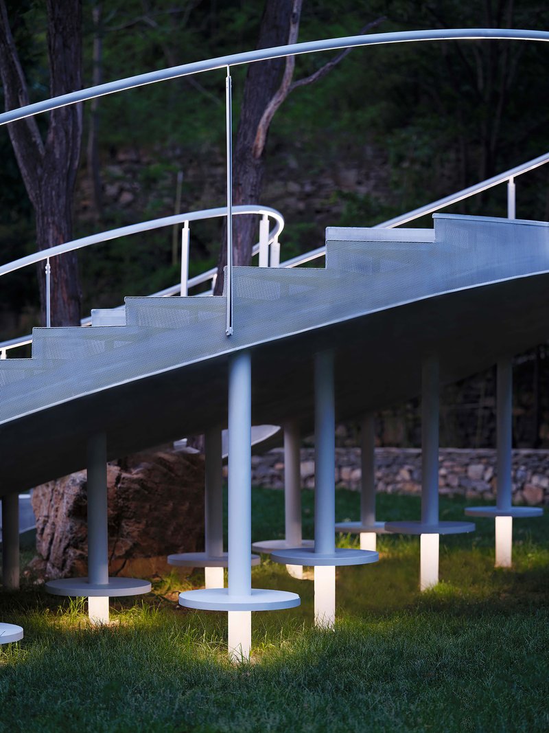 Illuminated cylindrical ground lights beneath the elevated stair platform at dusk