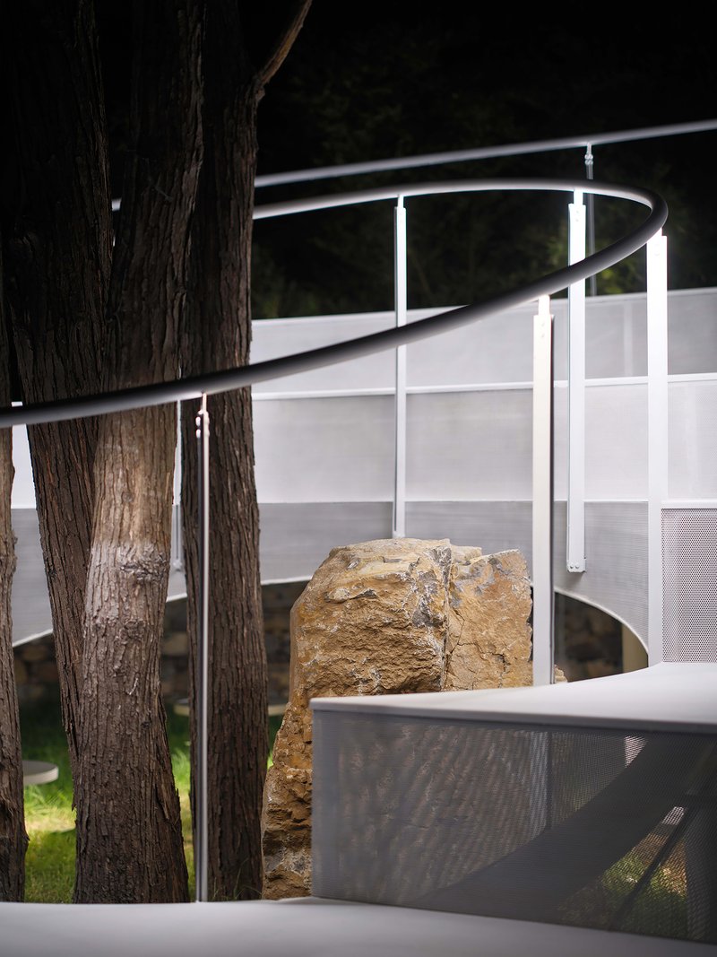 Close-up of tree trunks threading through white railings and mesh panels at night