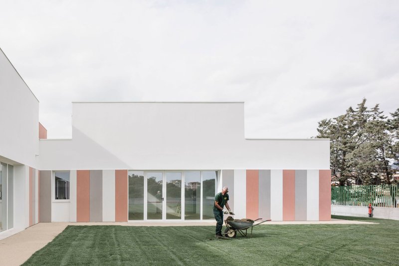 Vertically striped facade in white, grey and terracotta panels with a worker pushing a wheelbarrow on the lawn