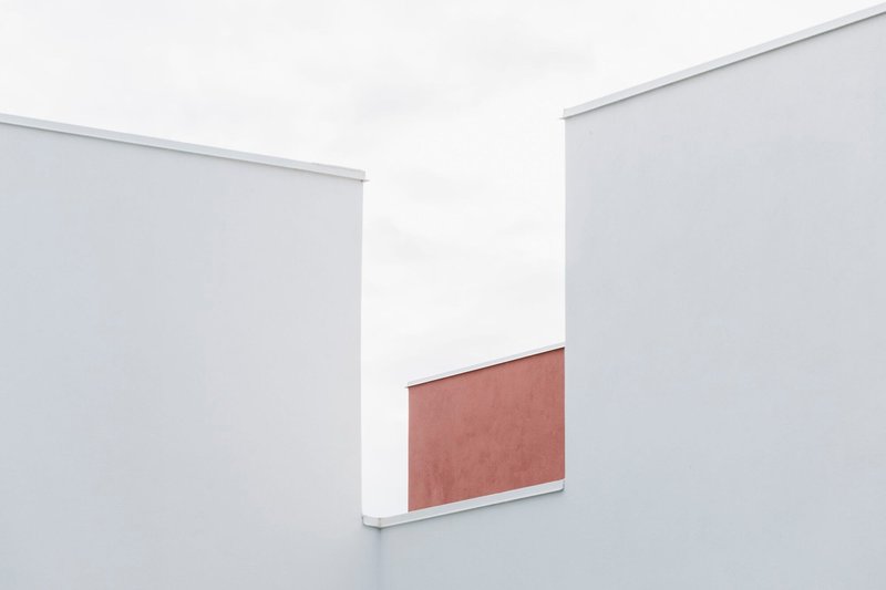 Abstract composition of white volumes with a terracotta panel glimpsed between them under diffused daylight