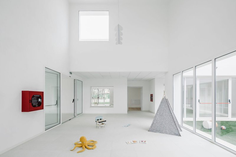 White interior room with floor-to-ceiling glazing, clerestory window, and scattered toys on polished concrete floor