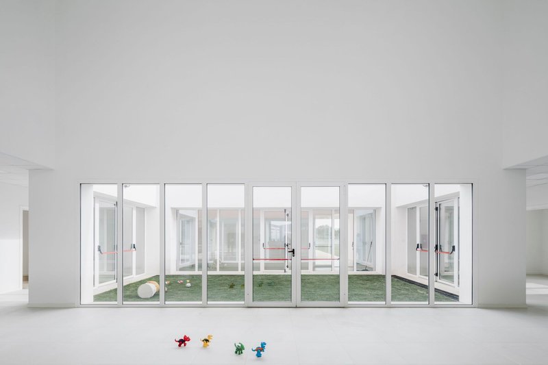 Interior view of nine-panel glazed wall opening to a courtyard with scattered plastic toys