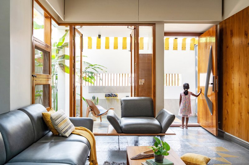 Living room with timber-framed glazing opening to a courtyard where a child stands by the door