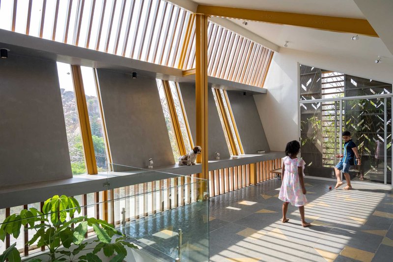 Upper hall with angled timber louvre clerestory casting striped light on two children walking across grey tiles