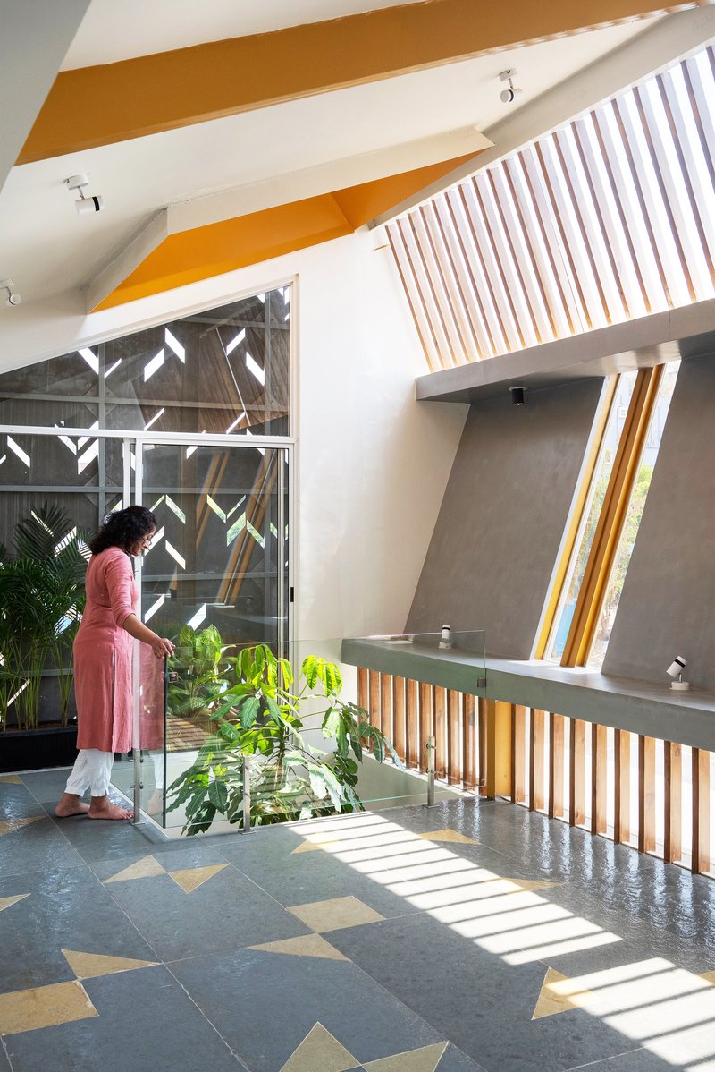 Interior courtyard with patterned floor tiles, timber slat screens, and a person in pink standing beside potted plants