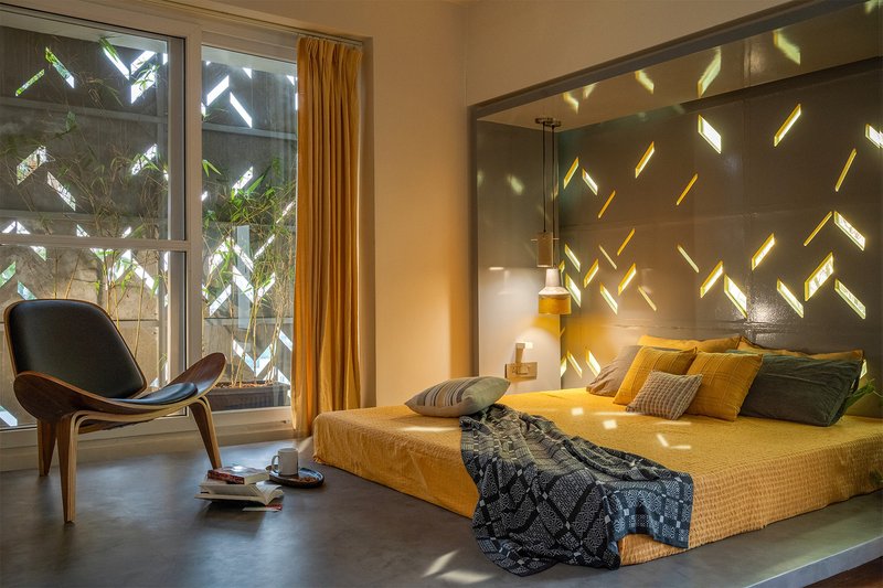 Bedroom with perforated concrete wall casting dappled light patterns across the bed and polished floor