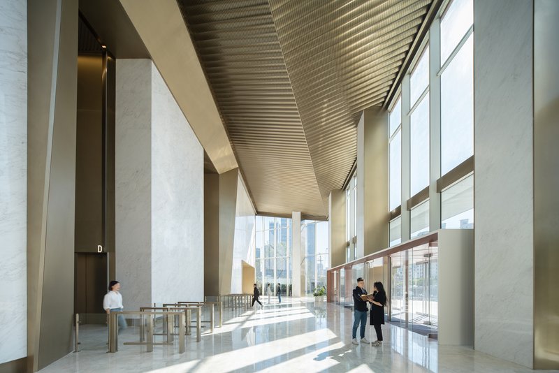 Interior lobby with ribbed metal ceiling soffit and stone-clad columns flooded with daylight