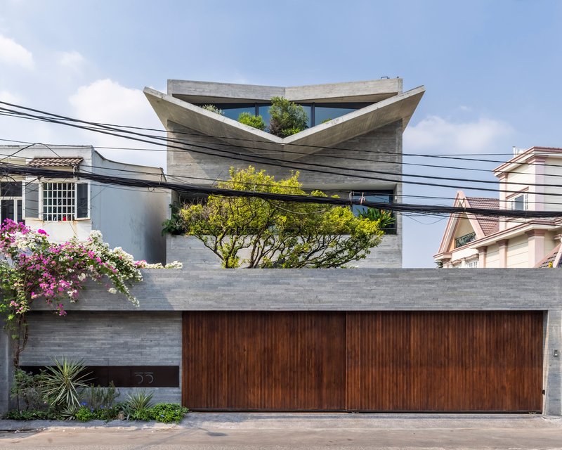Street view of the board-formed concrete facade with folded roof planes and vertical wood garage door