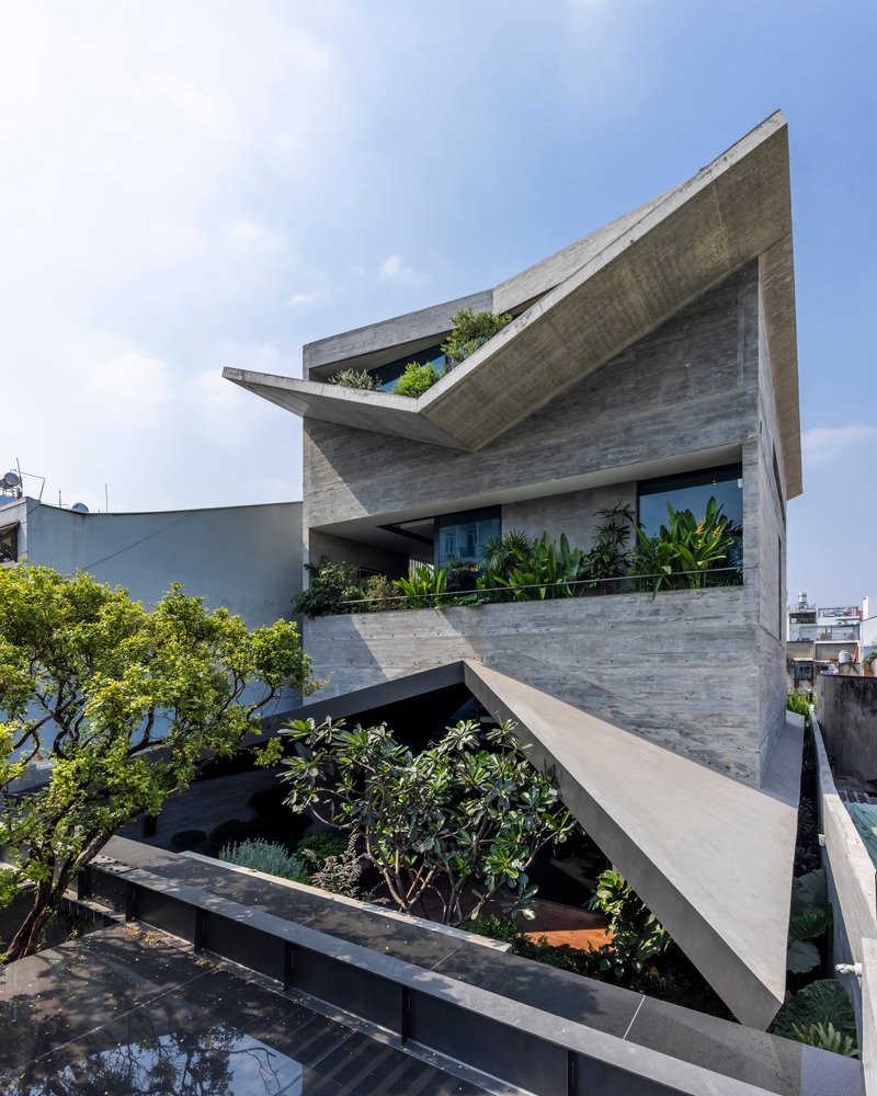 Angled facade showing planted terraces with trees and cantilevered concrete slabs under scattered clouds