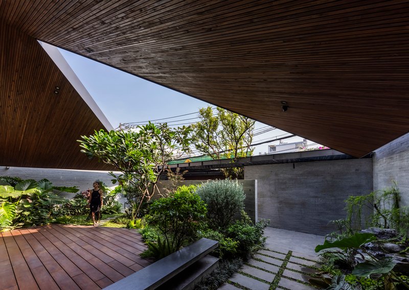Garden courtyard with timber decking and diagonal wood ceiling overhang sheltering a resident and planted beds