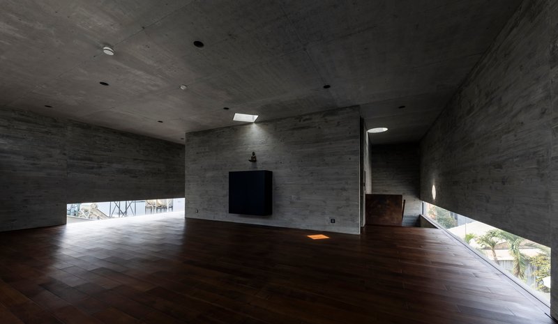 Double-height concrete interior space with dark timber flooring and horizontal strip windows