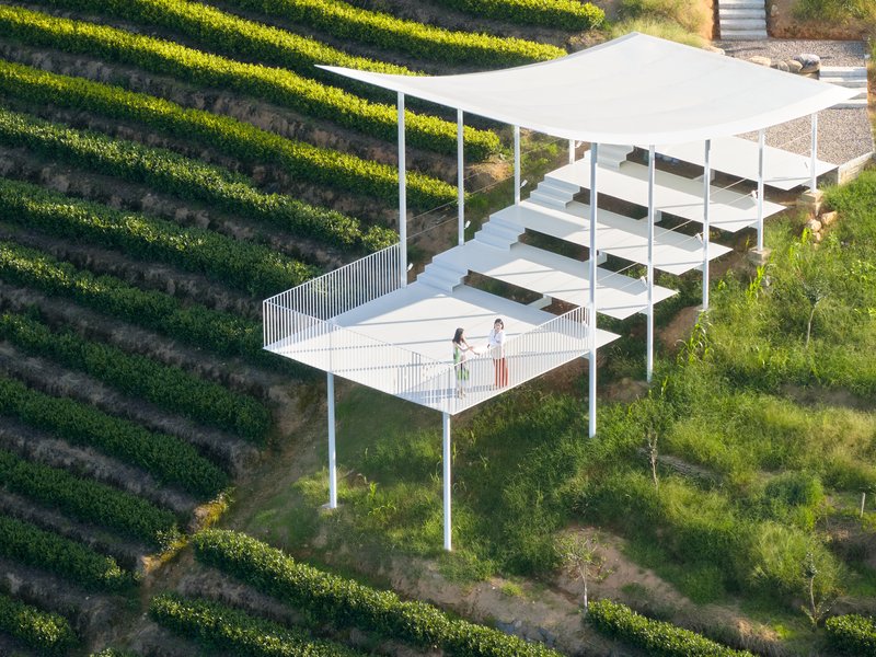 Aerial view of white steel pavilion with terraced platforms and vertical slat railing among planted slopes