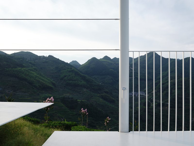 Vertical white railing and horizontal cable rails framing a view of green mountain slopes at dusk