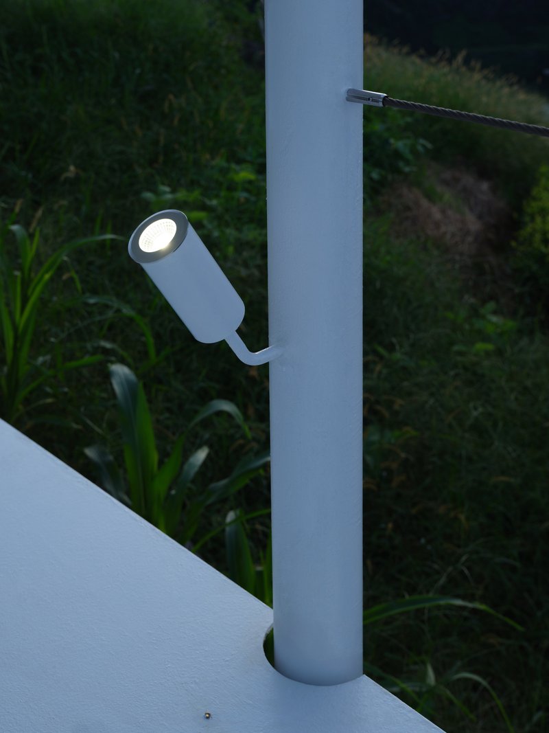 Cylindrical exterior light fixture mounted on a white column at twilight with vegetation beyond