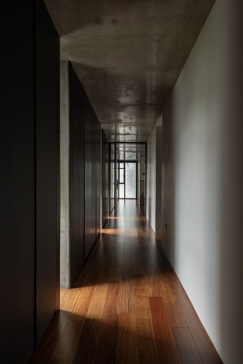 Narrow corridor with board-formed concrete ceiling and timber flooring leading to a glazed door