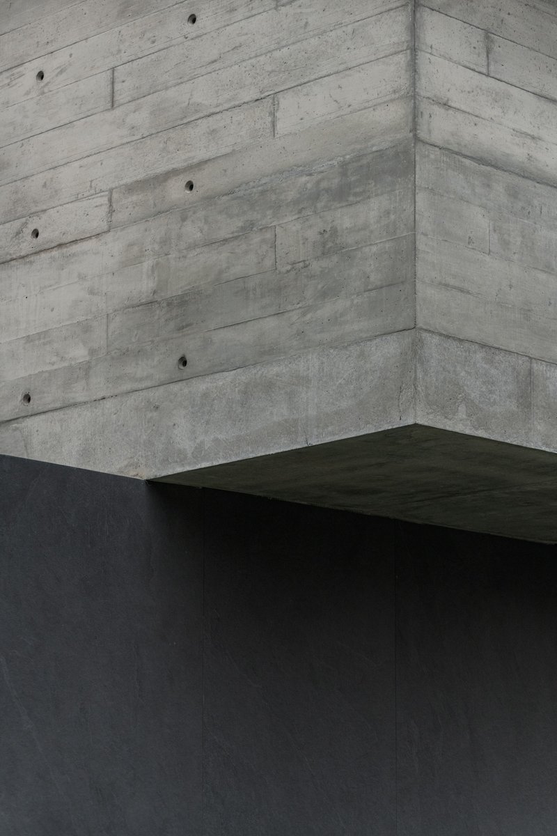 Corner detail of board-formed concrete walls meeting a dark cantilevered volume