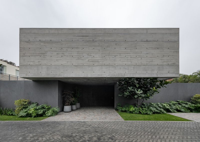 Street view of the cantilevered board-formed concrete volume above a recessed entrance with tropical planting