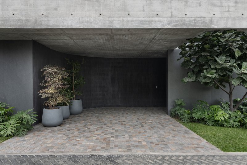 Covered entry with concrete ceiling and paver floor flanked by potted trees and lawn