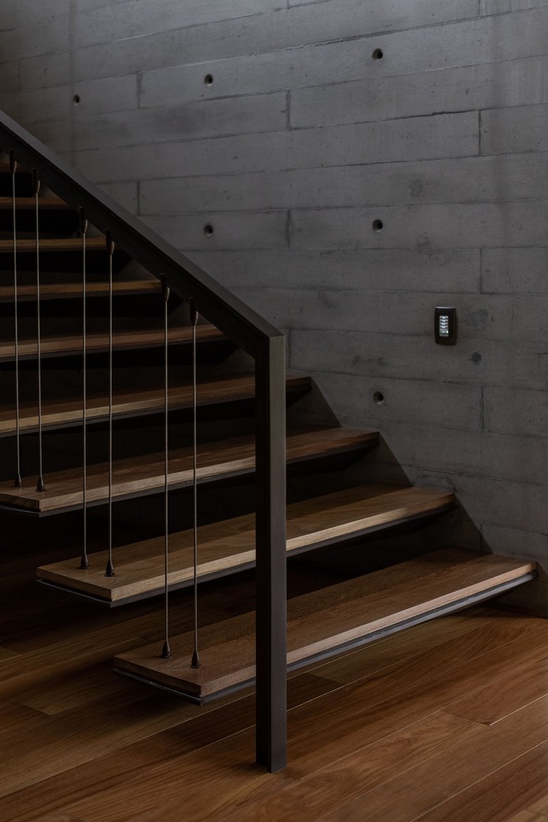 Timber staircase with steel cable railing against a board-formed concrete wall in low light