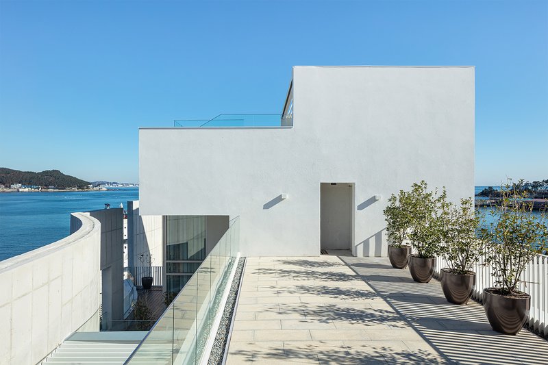 Rooftop terrace with white concrete paving and potted trees overlooking the harbor in midday sun