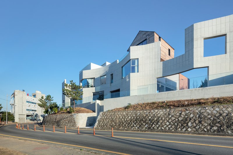 Street view of the clustered white panel facades atop a concrete retaining wall with diamond-patterned blocks