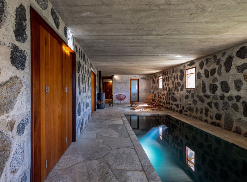 Poolside corridor with fieldstone walls and board-formed concrete ceiling casting shadows on flagstone paving