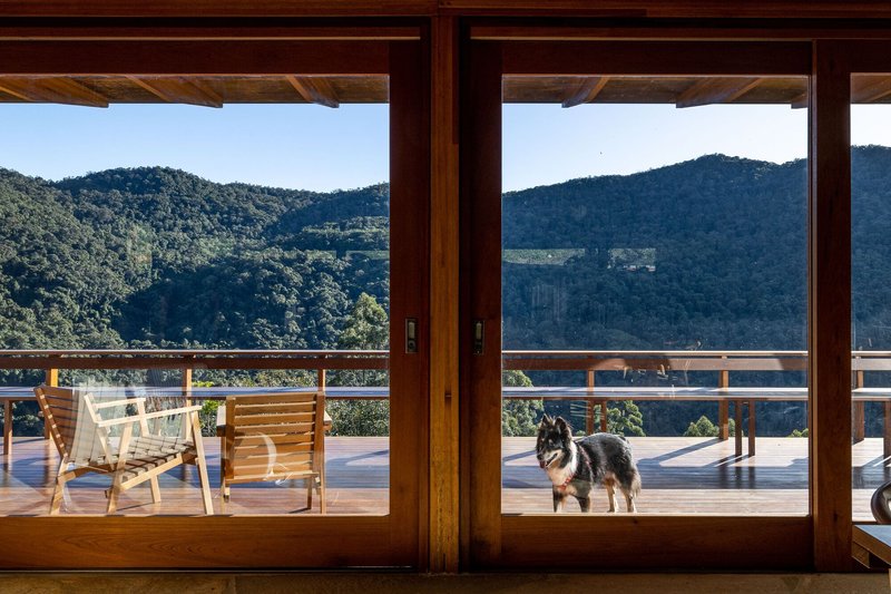 Timber-framed sliding doors opening onto a deck with outdoor seating and a dog beneath distant hills