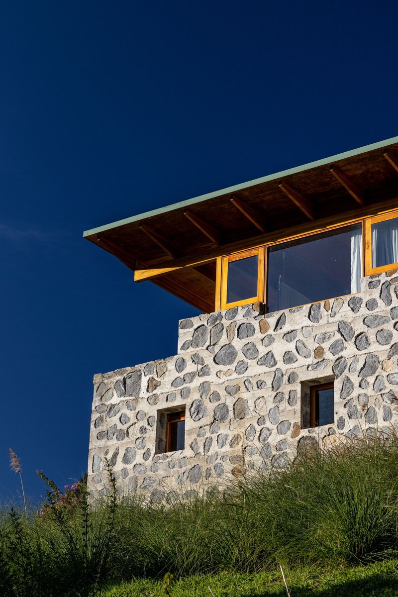 Upper level facade with river stone walls and timber roof overhang against deepening twilight sky