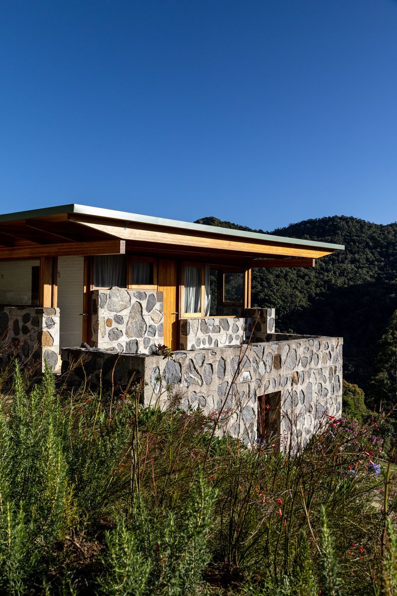 Two-level facade with river stone walls and timber framing surrounded by wildflowers under clear blue sky