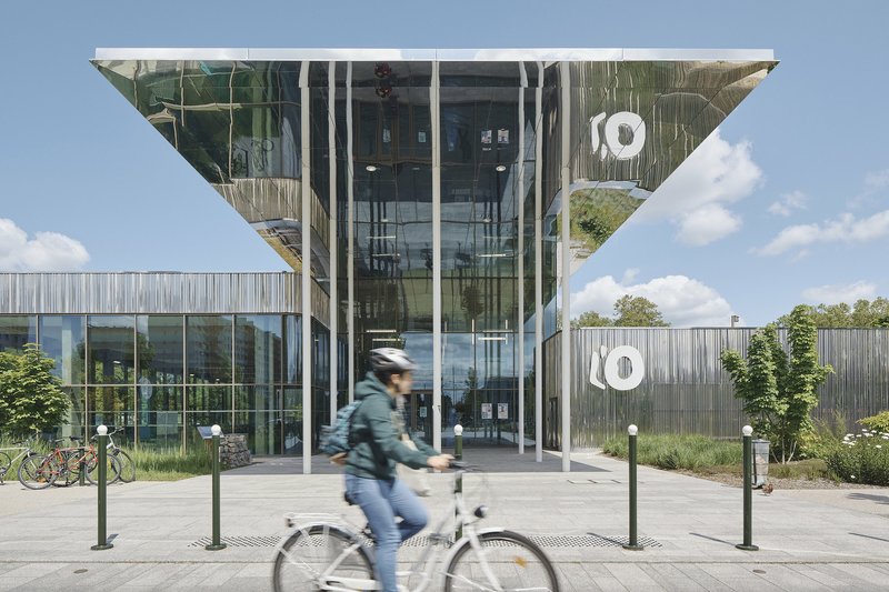 Glazed entrance with cantilevered soffit and cyclist passing on the paved plaza below