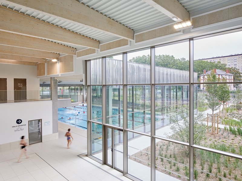 Interior hall with exposed timber beams and corrugated metal ceiling overlooking the swimming pool and planted courtyard