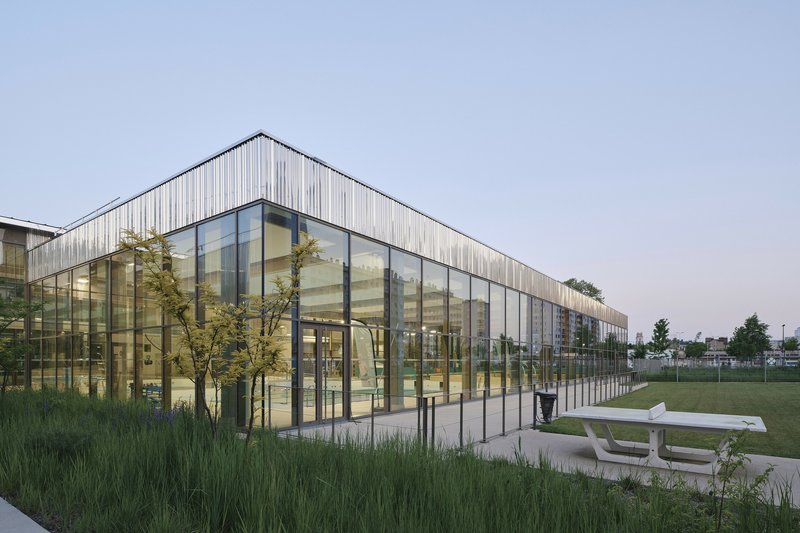 Corner view of the glazed facade and timber cladding at dusk with the adjacent lawn