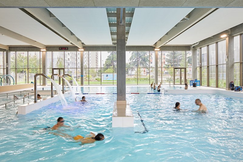 View across the pool to floor-to-ceiling glazing and a sunlit park beyond the water
