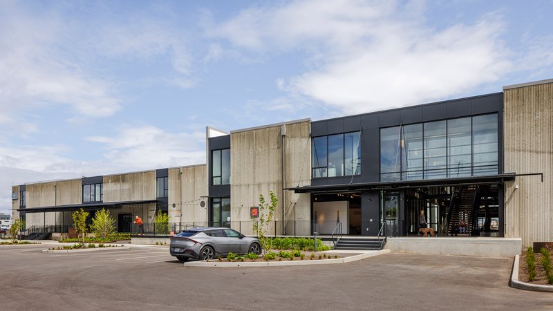 Street view of the two-storey facade combining light timber cladding and dark metal panels with a canopied entry