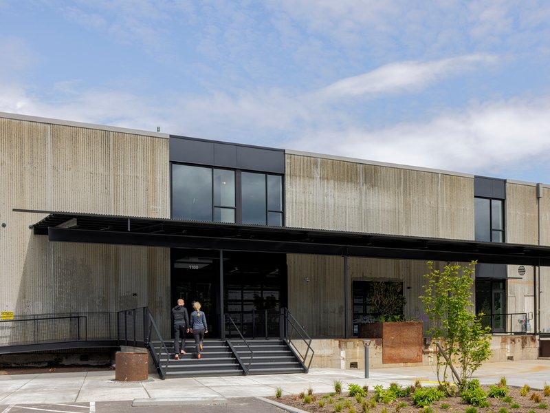 Front entrance with metal canopy, concrete steps, and weathered steel planters with two visitors ascending