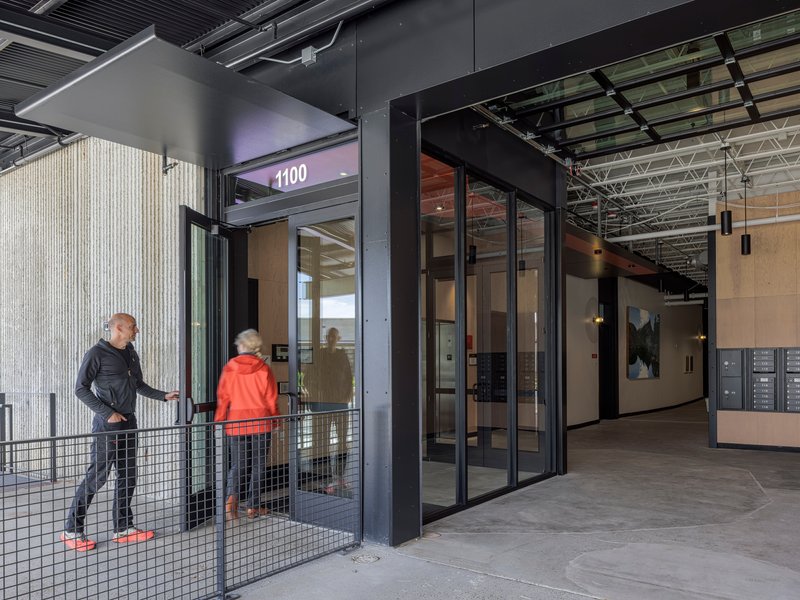 Mezzanine landing with metal mesh railings and glazed doors leading to numbered tenant spaces under exposed services