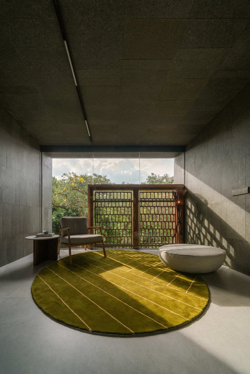 Concrete room with latticed timber screens framing the view and dappled sunlight on a green circular rug