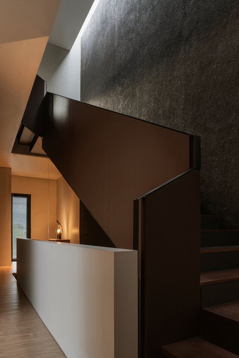 Dark timber staircase rising against textured concrete walls with warm light from below