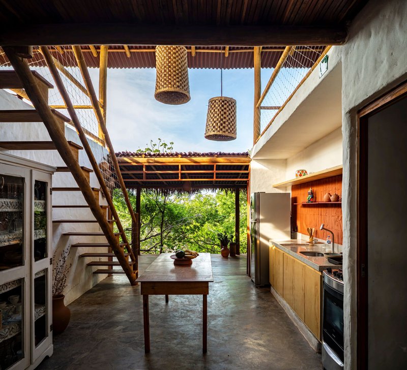 Interior kitchen with woven pendant lights and central table under a partial roof opening to sky