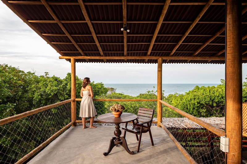 Upper terrace with rope railing where a person stands overlooking the ocean through coastal vegetation