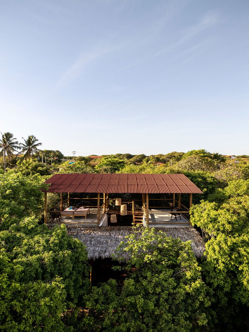 Frontal view showing the open-sided pavilion with red corrugated roof and timber columns among trees