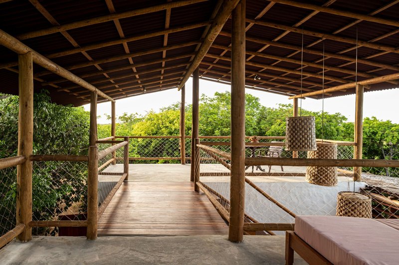 Upper-level terrace with timber columns, mesh railings, suspended woven lights and hammocks overlooking vegetation