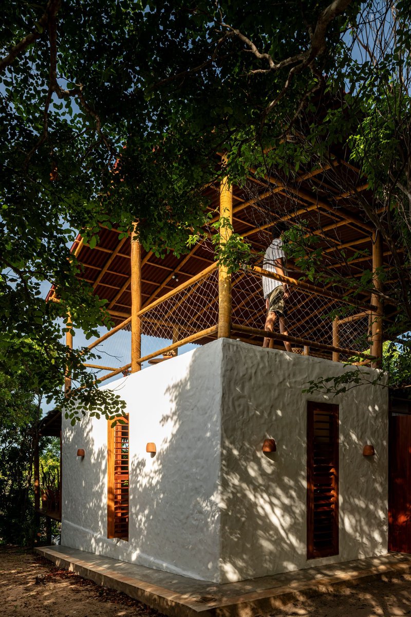 White rendered bathroom pavilion with timber-framed roof structure and lattice railing under dappled tree shade