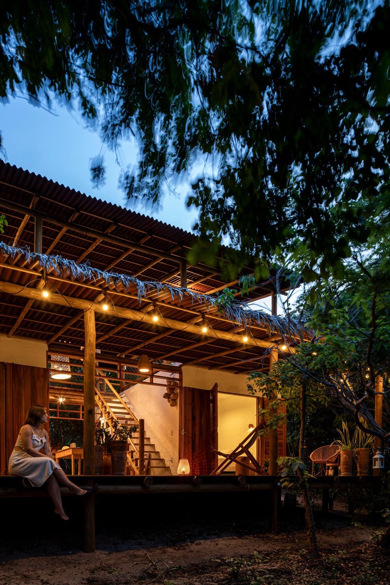Exterior porch with exposed timber roof structure and string lights at dusk beneath overhanging trees