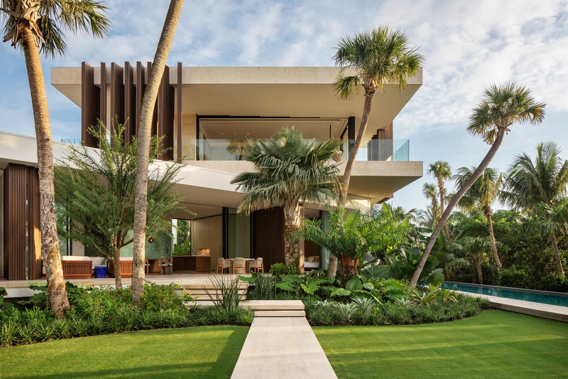 Garden view of the two-story residence with vertical timber screen and horizontal concrete balconies among palm trees