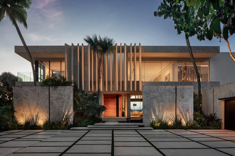 Entry facade with vertical timber louvres and stone walls illuminated at dusk beneath palm trees