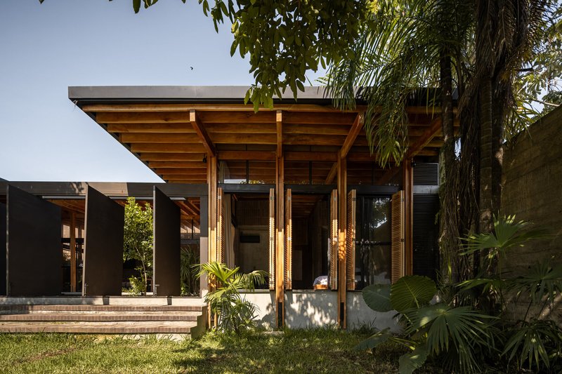 Timber pavilion with exposed rafters and slender columns framed by palm trees and lawn in afternoon light