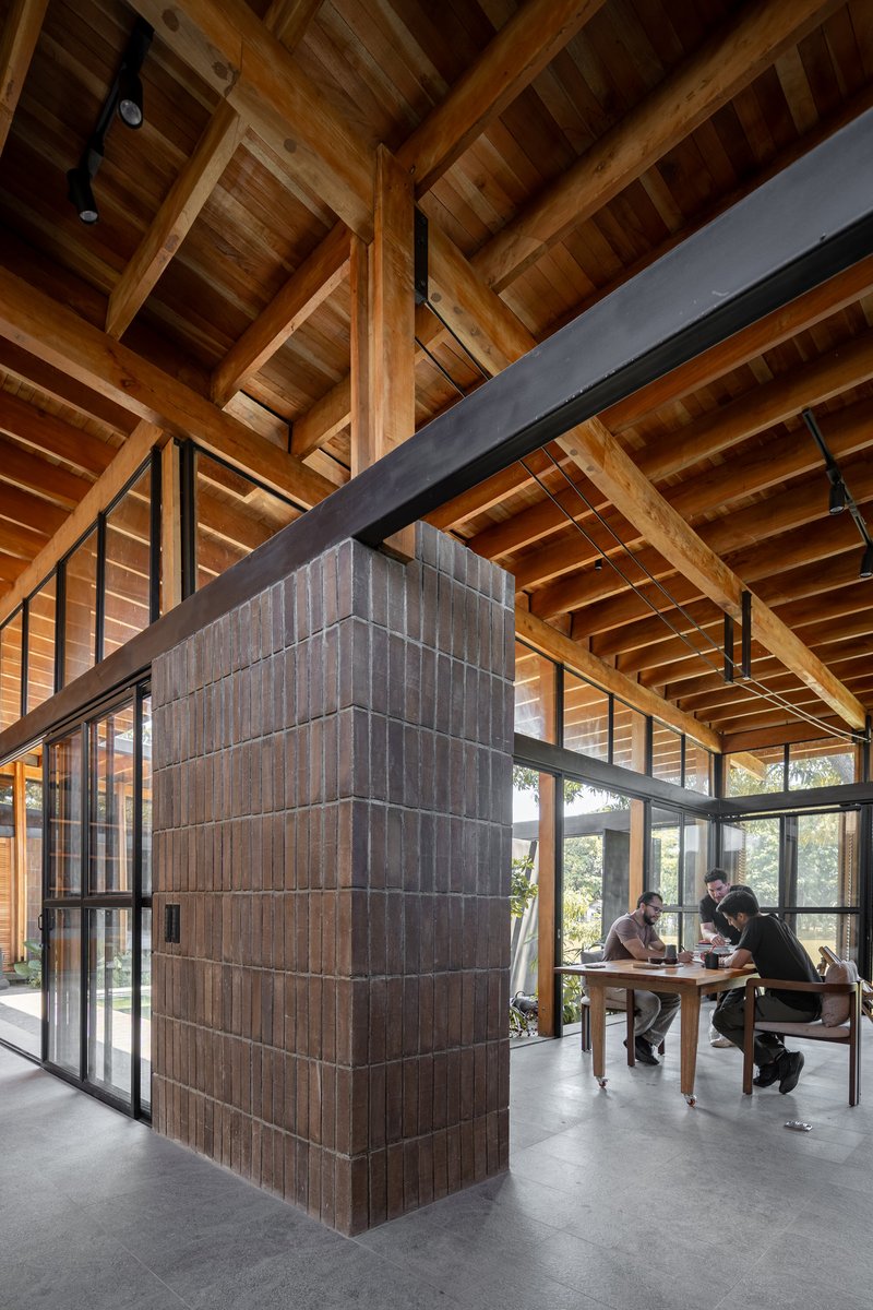 Vertical timber-clad core beneath crossing steel beams and a coffered wood ceiling with occupants nearby