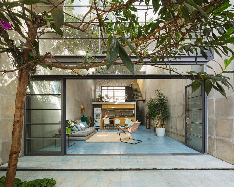 View from the planted courtyard through fully opened steel-framed glass doors into the double-height living space