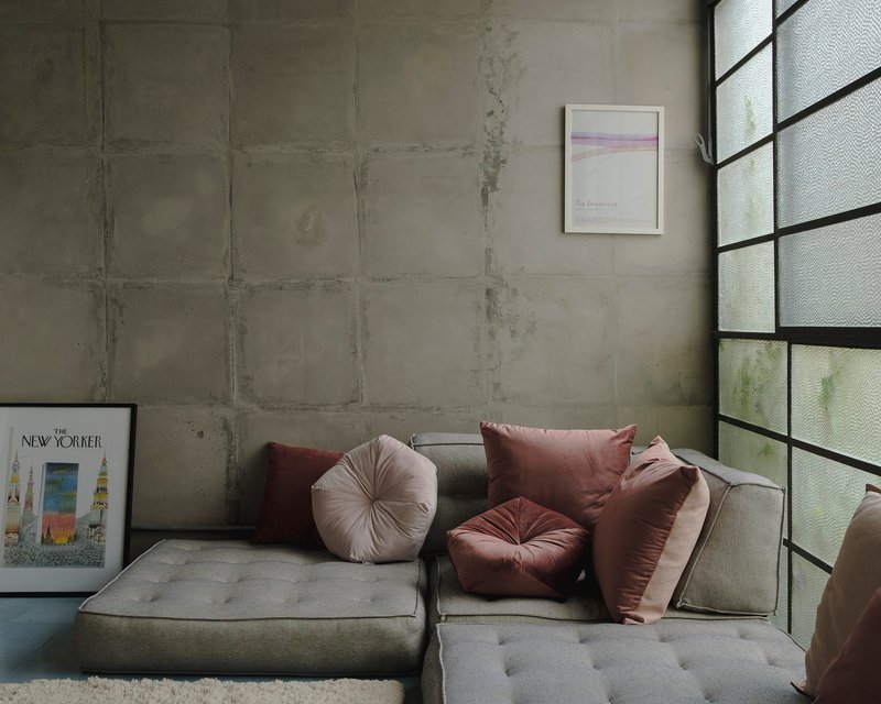 Corner seating area with board-formed concrete wall and translucent glass block window above grey sectional sofa